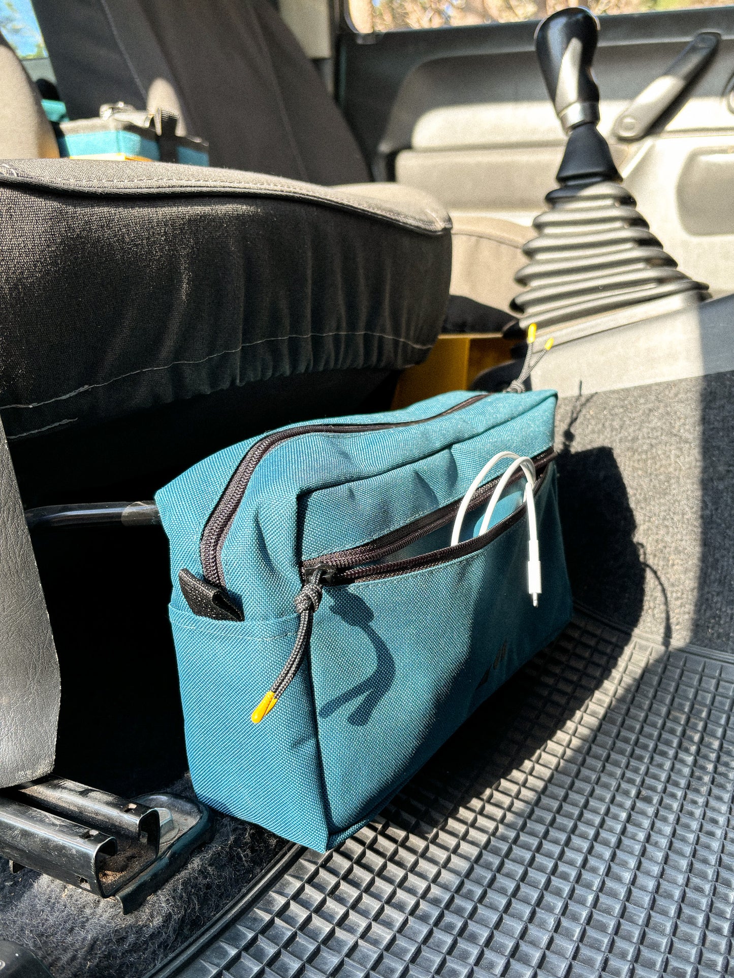 Anywhere Pouch in Teal, with front pouch unzipped, mounted on a Jimny 3 seat adjuster bar
