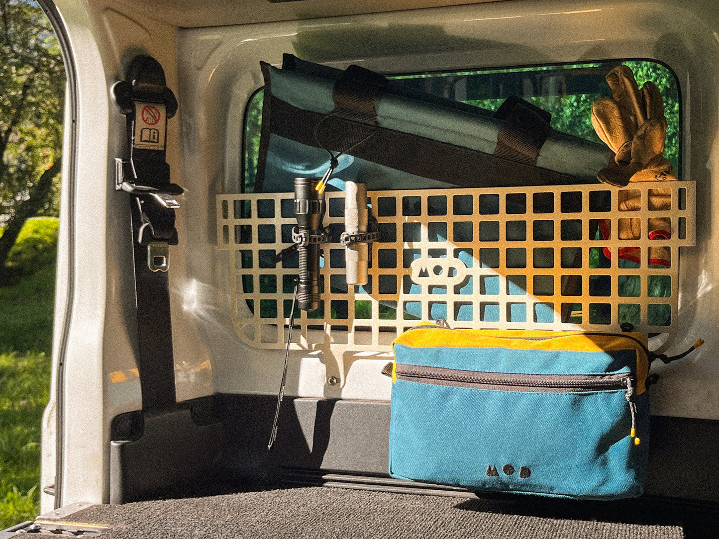 Back of a Suzuki Jimny with camping gear including a molle panel, blue bag, gloves, and other supplies.