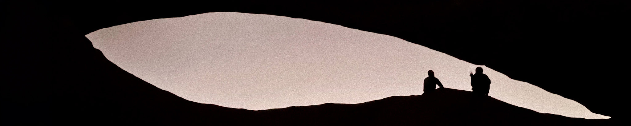 Two silhouetted figures sitting in The Bridge arch rock formation in Namibia's Spitzkoppe