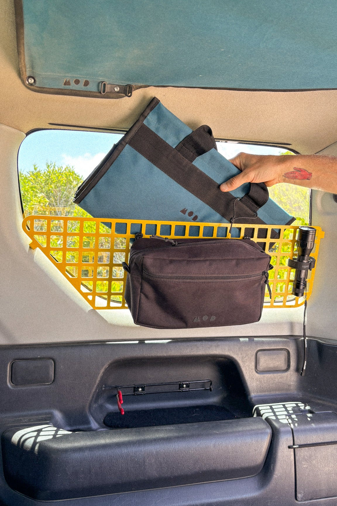 Hand placing a folded bag into a Jimny 3 Molle storage compartment 